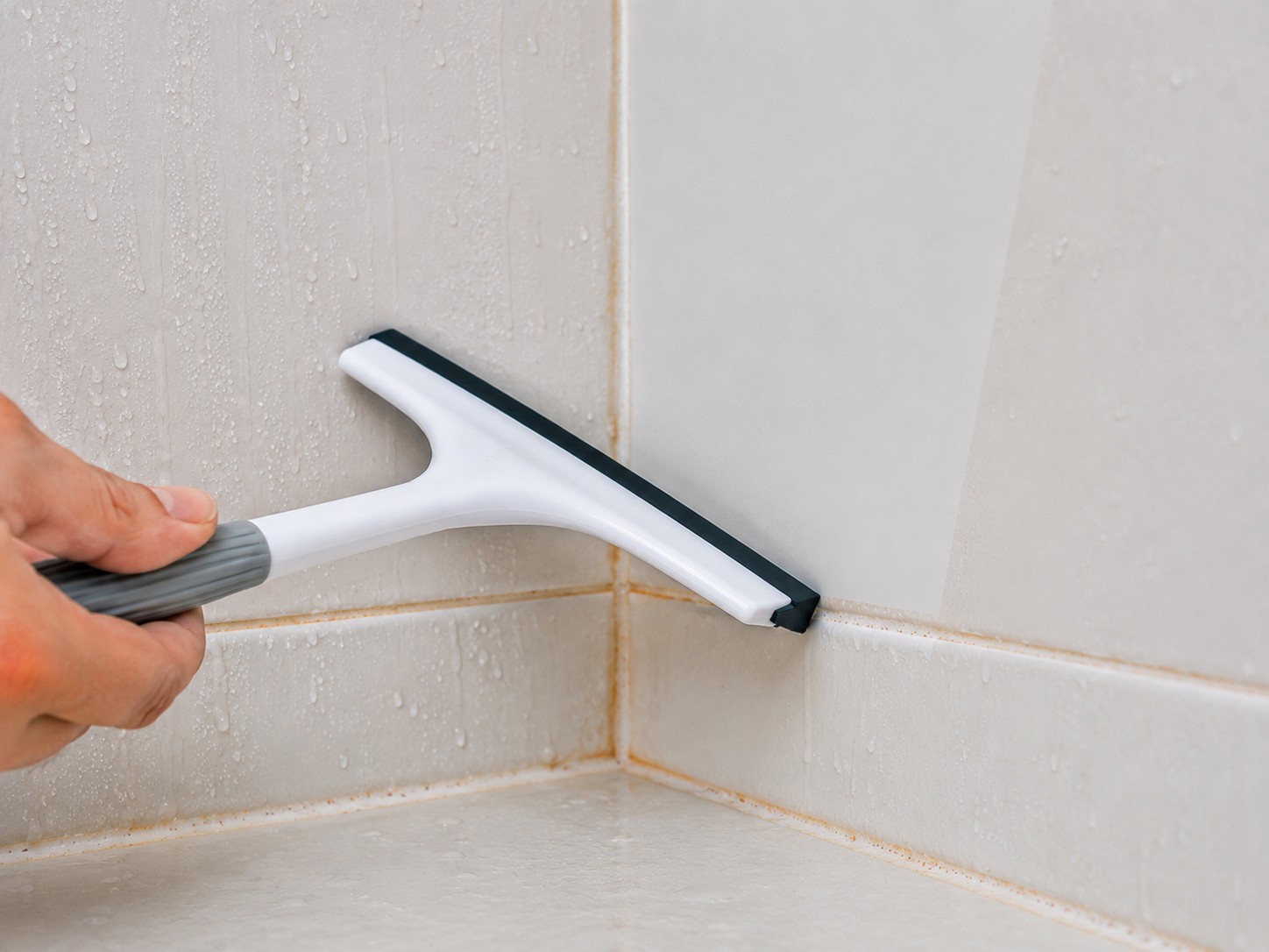 Squeegeeing shower walls to prevent orange grout stains from returning
